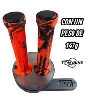 Puños de caucho TONYBIKESGDL naranja y negro con textura acanalada y tapones, pesando 147 gramos en báscula digital.